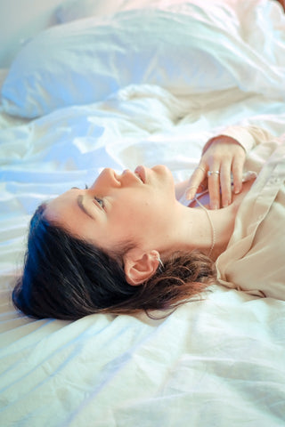 A woman lays in bed, surrounded by white bedding, staring up at the ceiling.