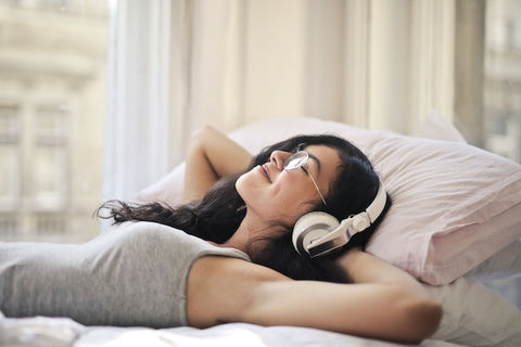 Woman wears headphones while laying in bed