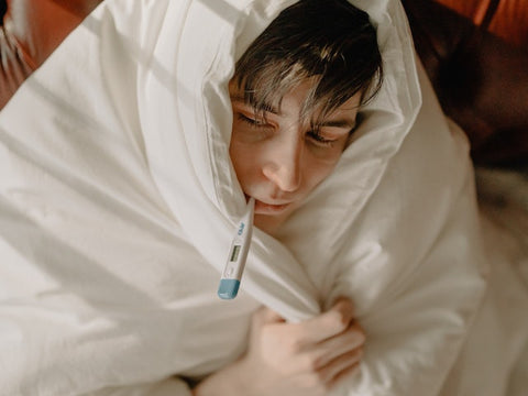 A sick man takes his temperature while wrapped in a blanket.