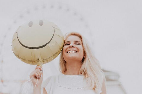 A woman poses with a smiley face balloon, showcasing her joy and happiness.