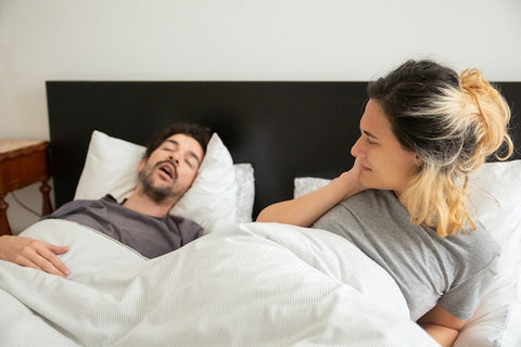 A man snores in bed, disrupting his sleeping partner. 