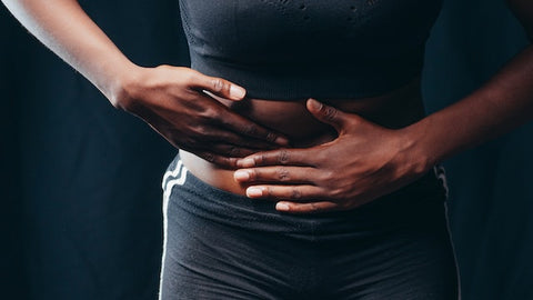 A woman in black active wear holds her stomach.