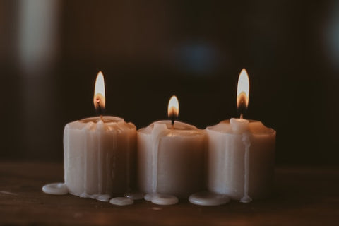 Three white candles sit lit on a surface with wax melting down.