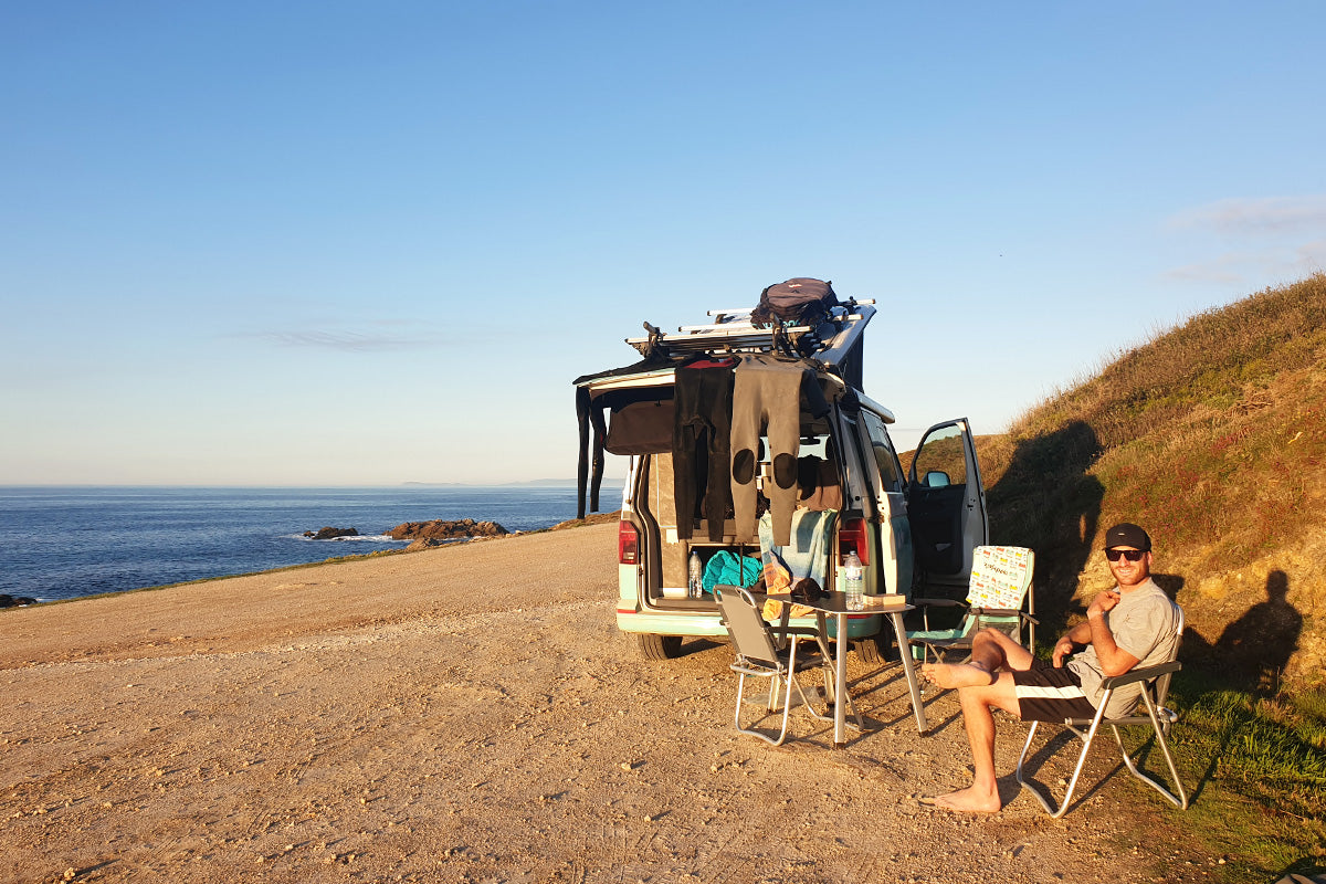 Ben sits in the sunshine by the beach outside a camper van