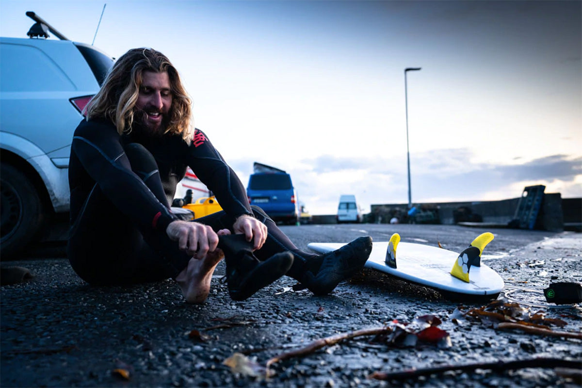 surfer wade carmichael pulling on his wetsuit boots in a beach car park