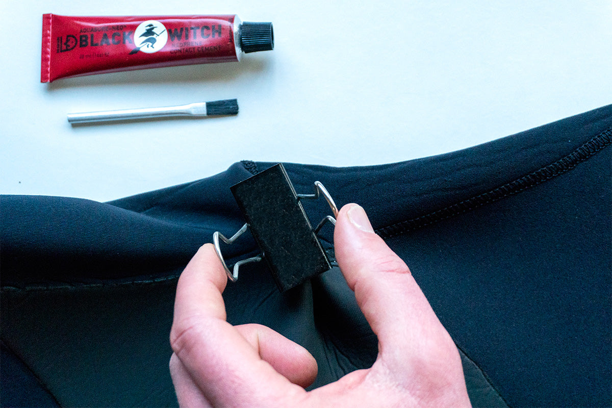 using a bulldog clip to secure a wetsuit repair whilst the glue dries