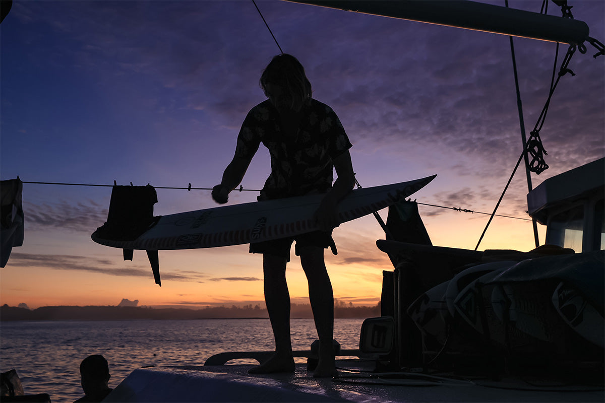 silhouette of surfer billy kean at sunset on a boat in indonesia