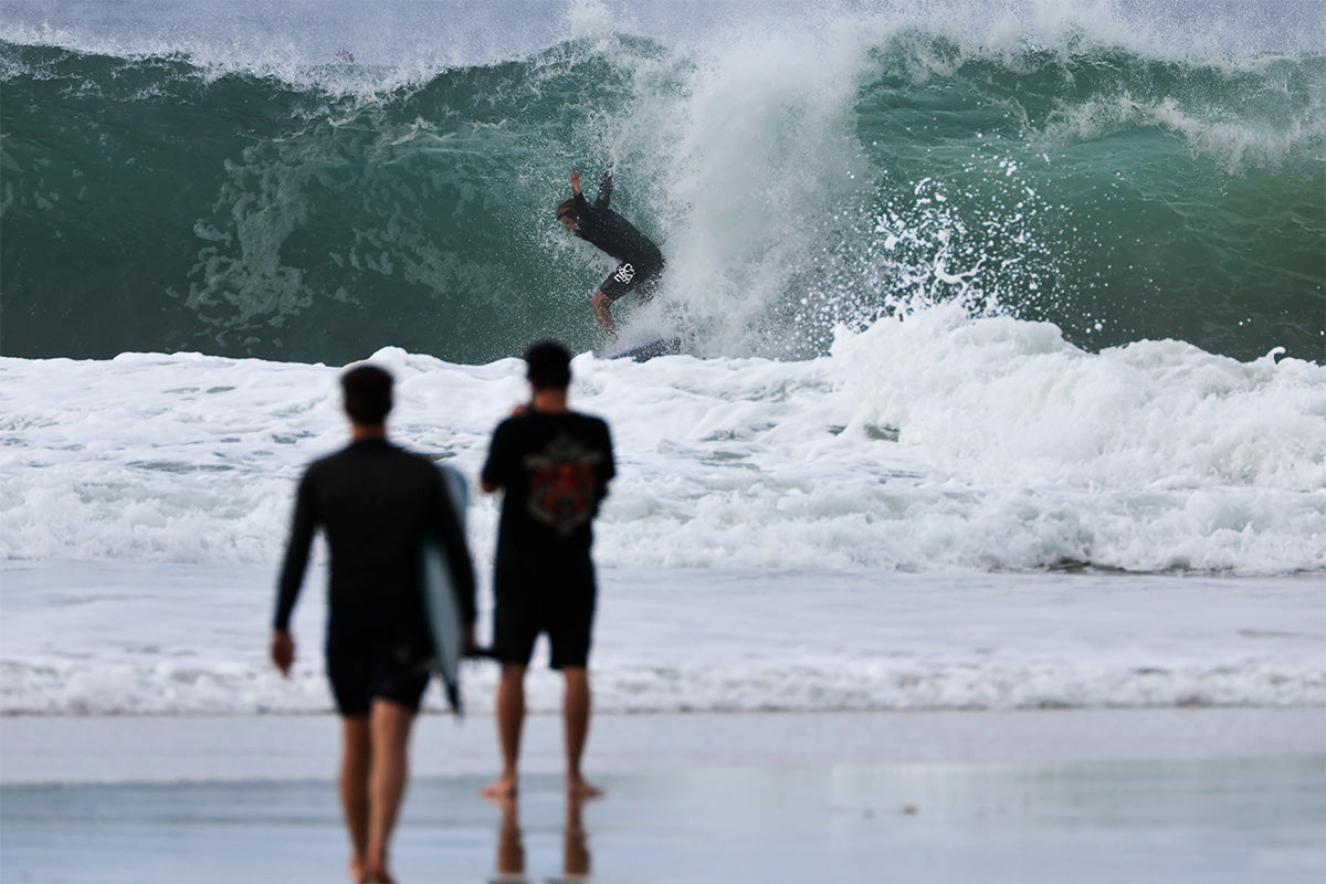 surfer wade carmichael air dropping into a hollow wave at snapper rocks with two surfers looking on from the shore, photographed by swilly