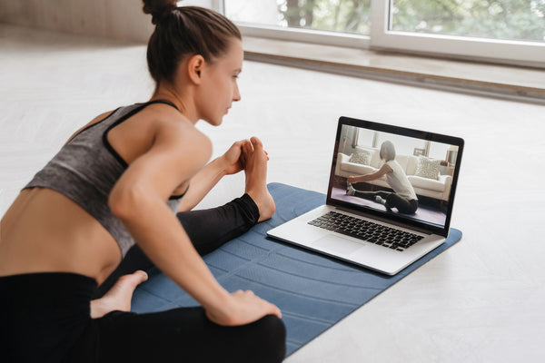 Woman sitting on the floor training yoga in front of a laptop