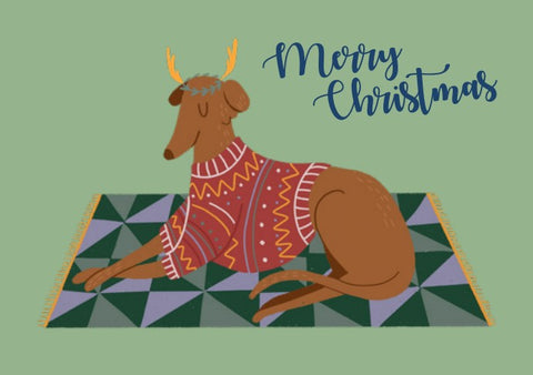 Charity Christmas Card of a Greyhound / Lurcher / Whippet dressed as a reindeer on a rug.