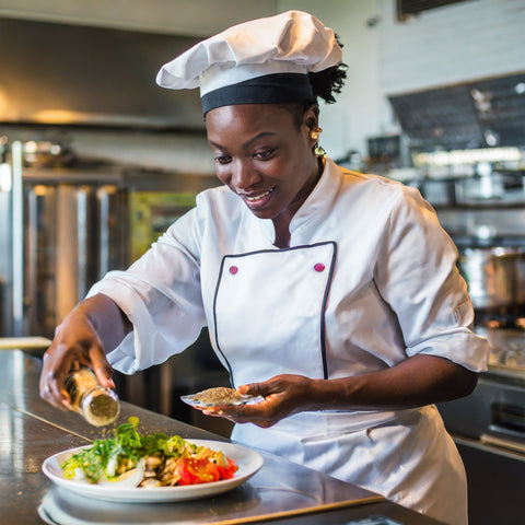 Woman seasoning food in a restaurant kitchen