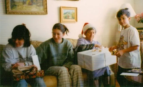 A family sits on a couch watching gift opening on Christmas morning