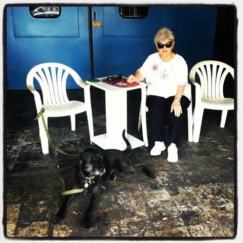 A woman in a garage sitting on a white plastic chair. A black dog lies near her