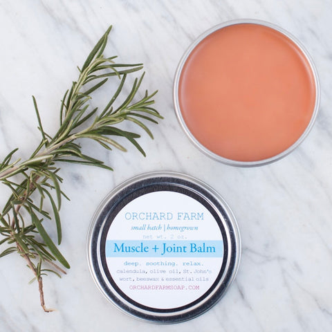 Open tin of muscle and joint balm on a marble with a sprig of rosemary