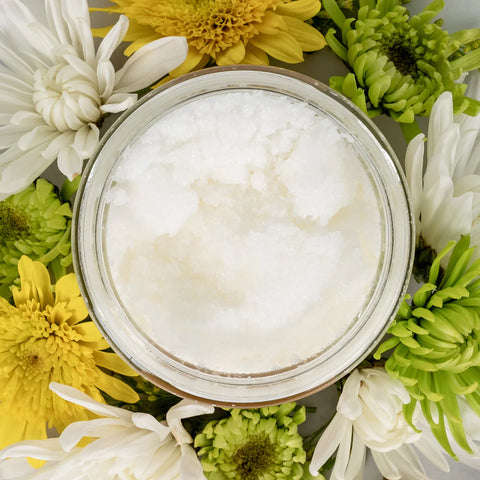 birds eye view of glass jar filled with salt scrub. Jar is surrounded by white, yellow and green flowers.