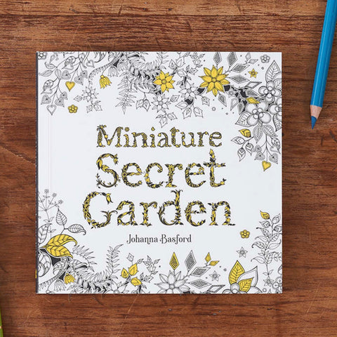 Miniature secret garden coloring book on a wooden table with a blue pencil in the upper right corner