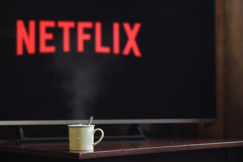 A television in the background has the Netflix logo on the screen. A steamy mug sits on a coffee table in the foreground