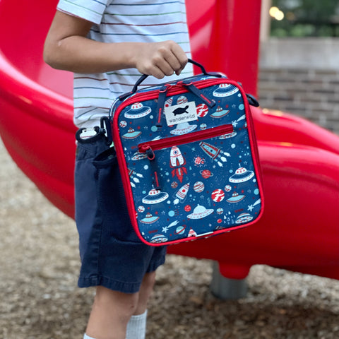 Child Holding Out To Lunch Blast Off lunchbox in color blue with rocket ship pattern while standing on playground