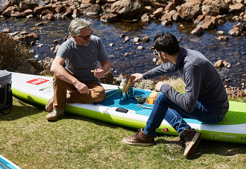 2 Men Eating While Sat On A Red Paddle Board
