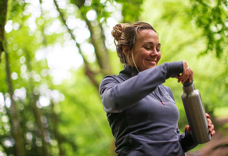 Drinking from an insulated water bottle in a forest