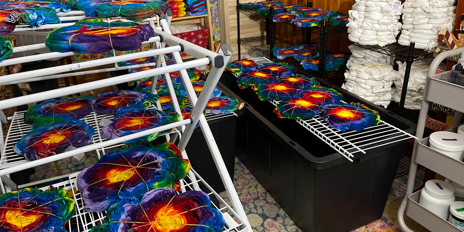 Dozens of rainbow sunburst tie dye tees in progress for a large custom order request, filling the entire studio workspace