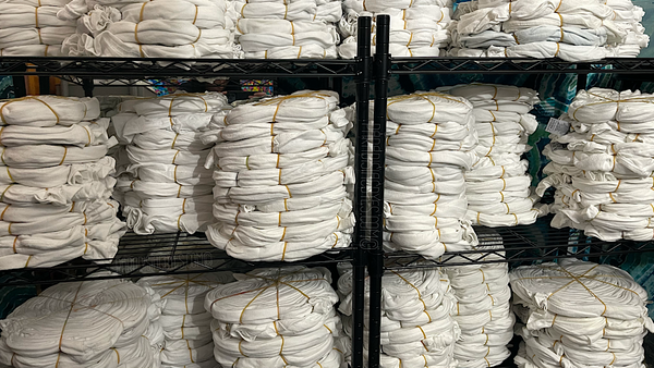 Hundreds of blank white spirals stacked in piles on wire shelving units as they prepare to be tie dyed for a large custom commission