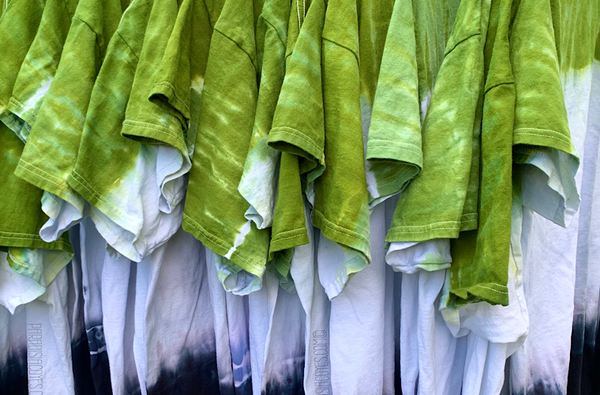 Over a dozen custom made horizontal striped, gradient design tie dye shirts, featuring green and black with a white center, hanging on a clothing display rack