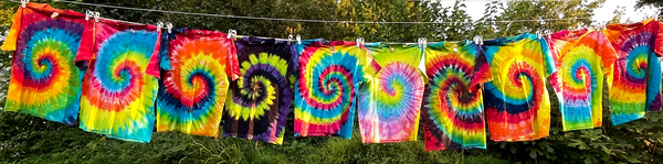 Vibrant neon rainbow spiral tie dye t-shirts hanging side by side outside on a clothesline.