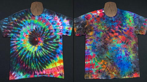 Two different blackened rainbow ice dyed tees side by side; on the left is a black spiral with rainbow colors inbetween, to the right is a marbled watercolor rainbow splatter pattern