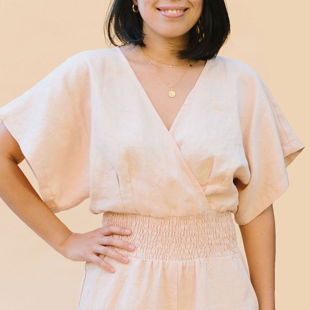 A close up of a woman wearing a peach jumpsuit with a cross over bodice, pleats and a shirred waistband 