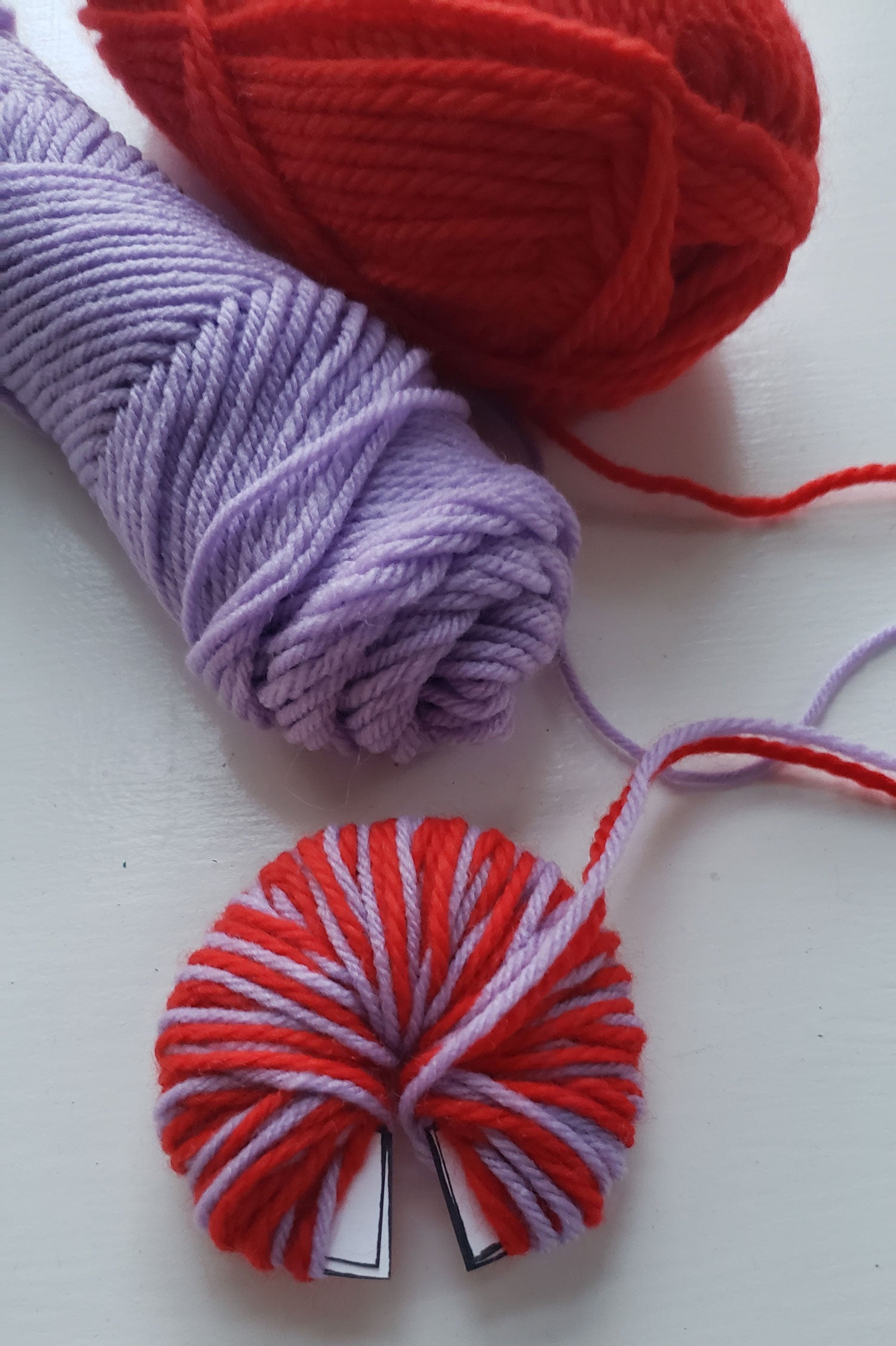 Red and purple yarn is being wrapped around a circular disk