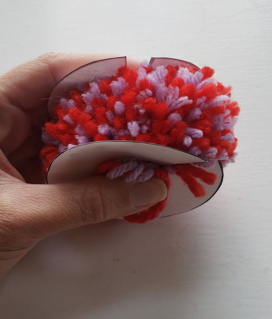 A pom pom sandwiched in between two pom pom maker disks