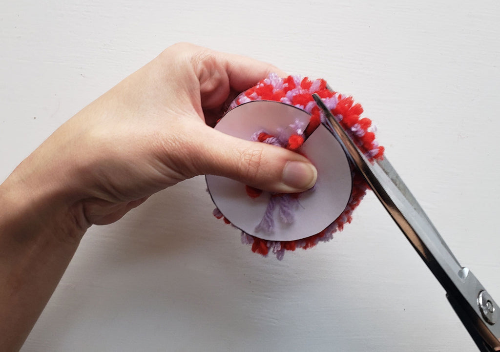 A pom pom is being trimmed with a scissors