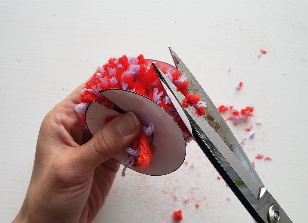 A pom pom is being trimmed with scissors