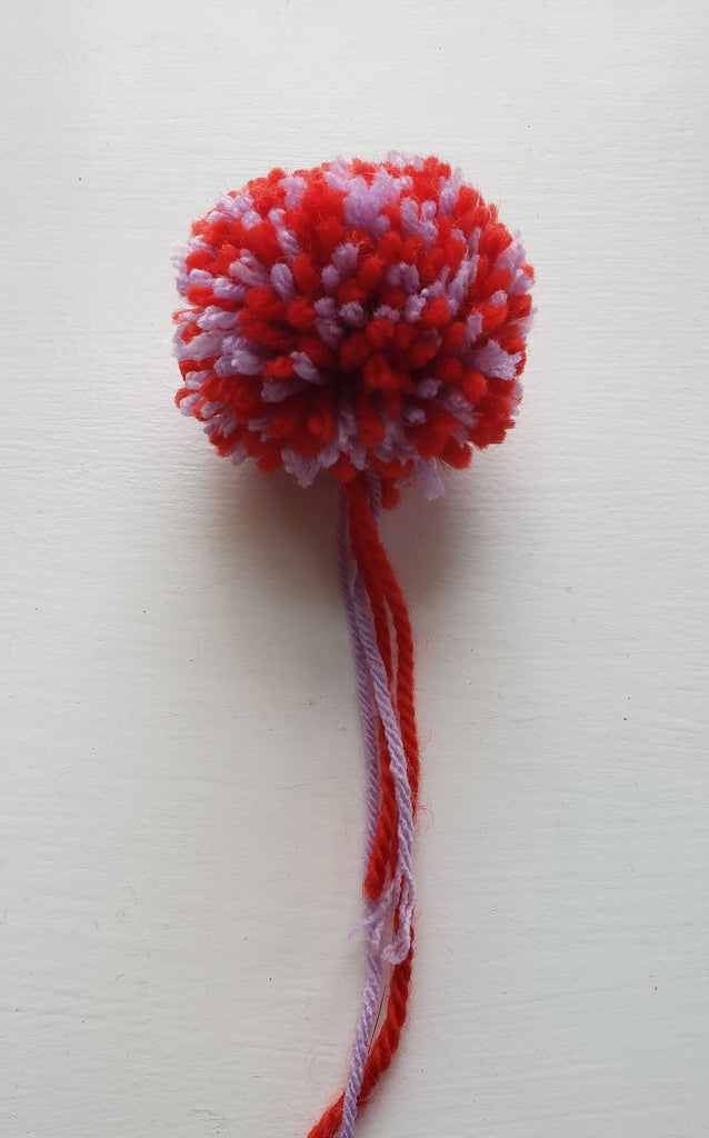 A red and purple pom pom with thread tails