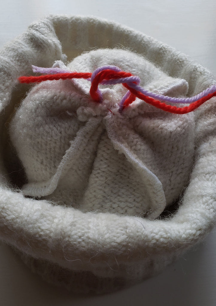 Knot being ties on the wrong side of a winter hat which will secure a pom pom