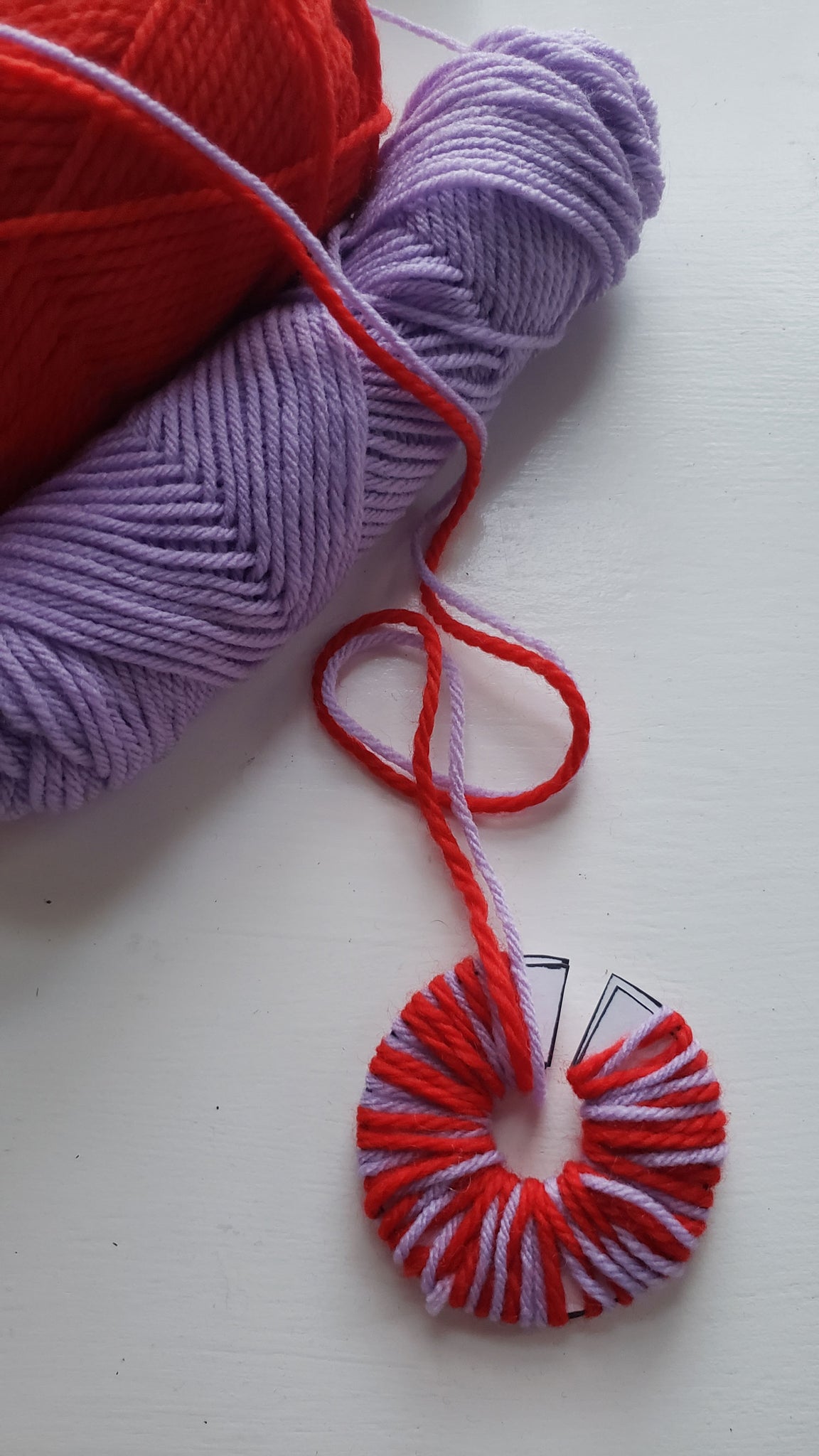 Red and purple yarn is being wrapped around a circular disk