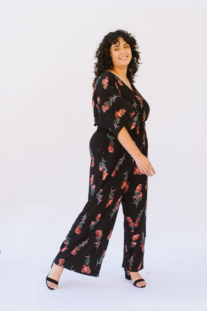 A woman stands twirling wearing a black floral print jumpsuit