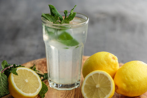 Glass of lemon water with water and mints around it