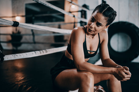 Woman resting by sitting on boxing ring after workout