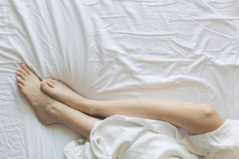 relaxing woman's legs half covered with white linen flat sheet laying on top of white linen fitted sheet