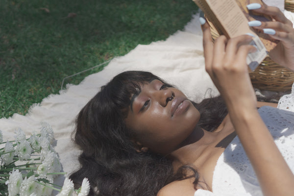 Ayune hair - Ethical hair extensions (Black woman laying in a garden reading a book)