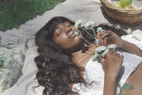 Ayune hair - Ethical hair extensions (Black woman laying in a garden smelling flowers)