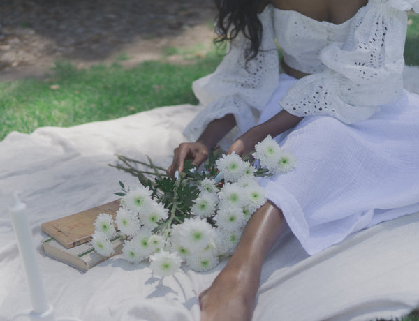 Ayune hair - Ethical hair extensions (Black woman sitting in a garden with flowers next to her feet))