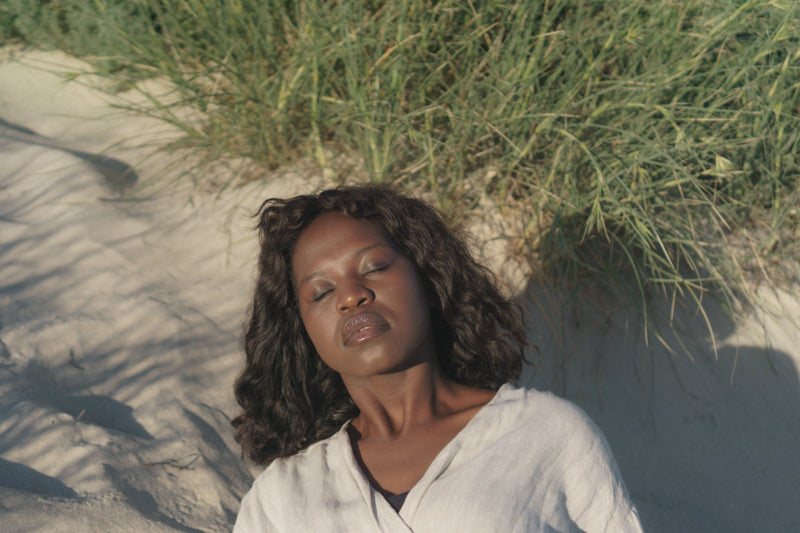 A close up shot of a Black woman laying on the sand with her eyes closed
