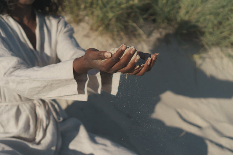 A Black woman holding sand in both of her hands as they slowly slip through her fingers