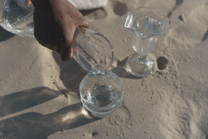 Black woman pour water in to two glass cups on the beach.