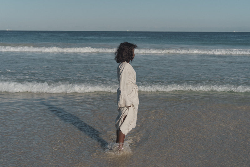 Black woman standing in front of the ocean. She is standing side-ways and looking away from the camera.