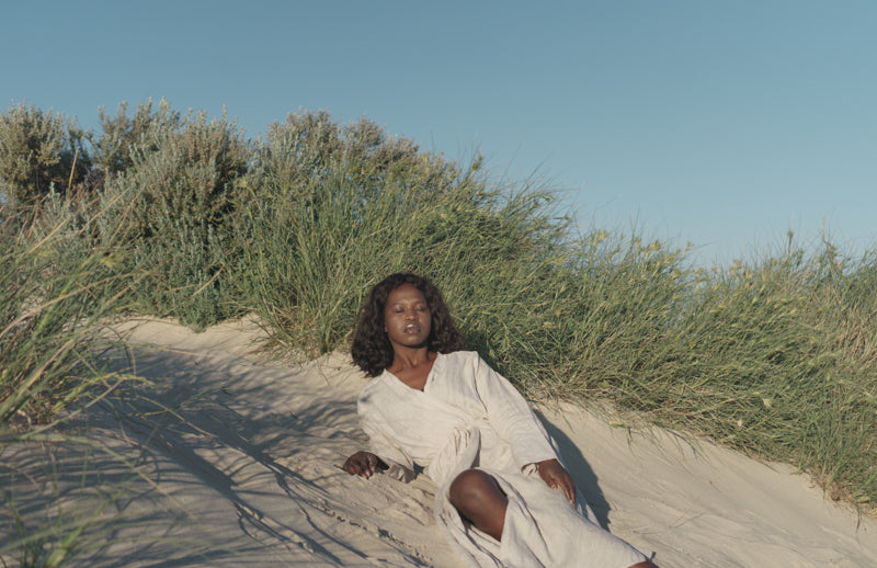 A Black woman laying on the sand with her eyes closed