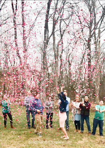 Couple posing with family and friends, while standing outside with pink confetti in the air.